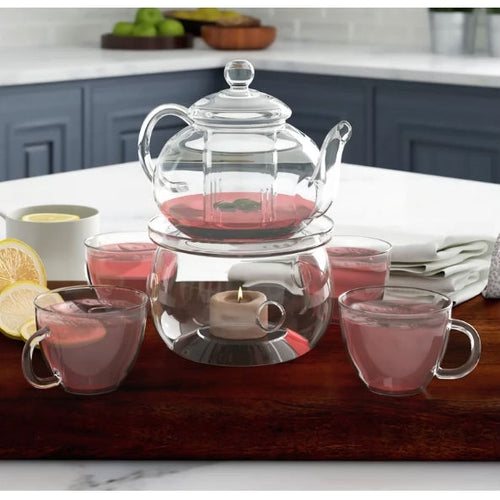 Clear glass teapot with pink liquid on a wooden tray in a kitchen setting

